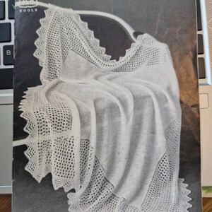 May include: A vintage book cover featuring a white, lacy shawl draped over a curved hanger. The cover has the text "TWO 2-PLY SHAWLS" and "II72-6d". The shawl has a detailed, openwork design.