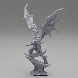 May include: A detailed, gray figurine of a winged demon warrior, posed dynamically on a rocky base. The figure has large, detailed wings, curved horns, and is wielding curved blades. The overall design suggests a fantasy or gaming theme.