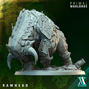 May include: A light gray miniature figurine of a beast with a large, armored ram-like head, curved horns, and mechanical plating on its shoulders. The base features the text PRIMAL WARLORDS and RAMHEAD, with the A Games logo in the corner.
