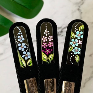 May include: Three glass nail files with black velvet cases. Each file has a different floral design with rhinestones. The designs are blue, pink, and light blue flowers.