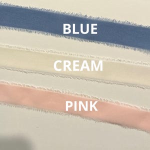 May include: Close-up of three ribbons in blue, cream, and pink. The word "BLUE" is above the blue ribbon, "CREAM" is above the cream ribbon, and "PINK" is above the pink ribbon. The ribbons have a frayed edge.