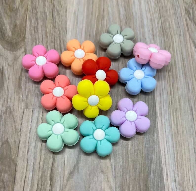 May include: Assortment of ten silicone flower-shaped beads in various colors, including pink, red, yellow, green, blue, purple, and gray. Each bead has a white center.