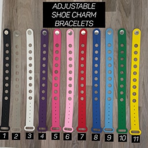 May include: Eleven adjustable shoe charm bracelets in various colors, including black, gray, white, purple, pink, red, blue, light blue, green, and yellow. The bracelets are numbered 1 through 11.