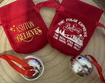 May include: Two red velvet drawstring bags with silver jingle bells. One bag says "Ashton Believes" in gold lettering. The other bag says "The Polar Express Believe" with a white train illustration and the text "The bell still rings for those who truly believe".
