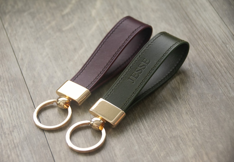 May include: Two leather keychains with gold rings and clasps. One keychain is burgundy and the other is dark green. The green keychain has the name "Jesse" embossed on it.