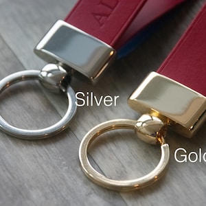May include: Two leather keychains with metal rings. The keychain on the left has a silver ring and the keychain on the right has a gold ring. The text "Silver" is below the left keychain and the text "Gold" is below the right keychain.