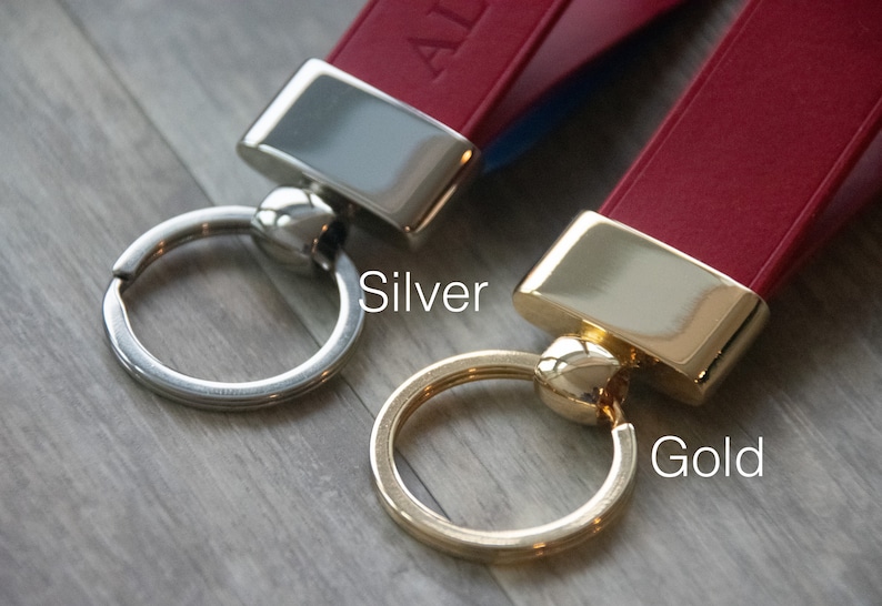 May include: Two leather keychains with metal rings. The keychain on the left has a silver ring and the keychain on the right has a gold ring. The text "Silver" is below the left keychain and the text "Gold" is below the right keychain.