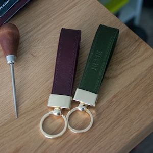 May include: Two leather keychains with gold rings. One is burgundy and the other is green. The green keychain has the name "Jesse" embossed on it.