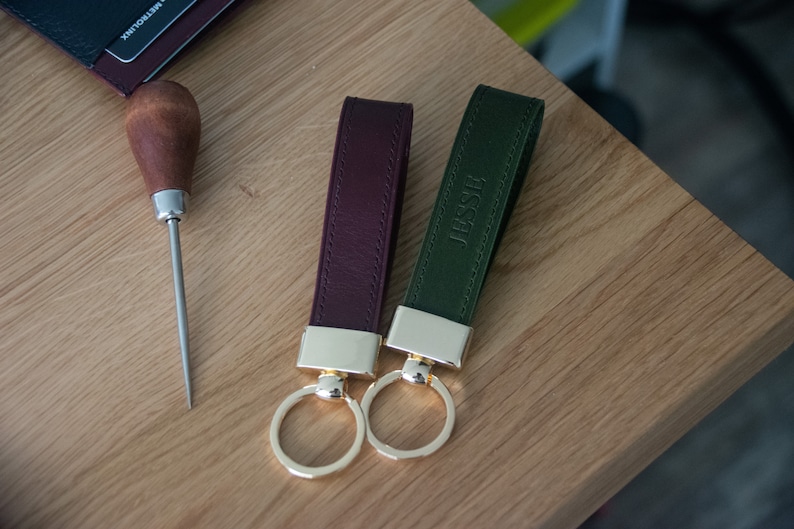 May include: Two leather keychains with gold rings. One is burgundy and the other is green. The green keychain has the name "Jesse" embossed on it.