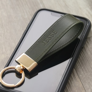 May include: A dark green leather keychain with a gold ring and a gold clasp. The keychain is personalized with the name "Jesse" embossed in the leather.