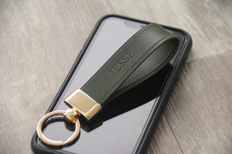 May include: A dark green leather keychain with a gold ring and a gold clasp. The keychain is personalized with the name "Jesse" embossed in the leather.