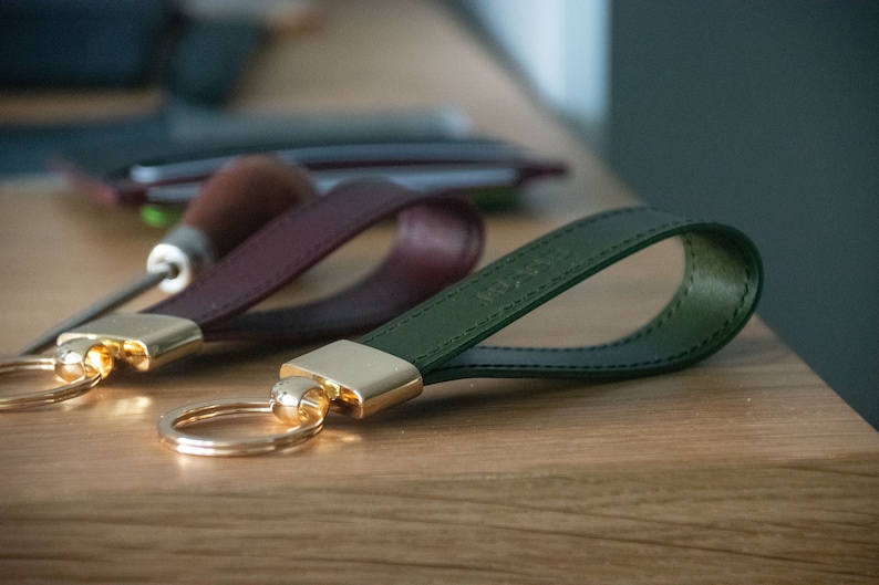 May include: Two leather keychains with gold key rings. One keychain is burgundy and the other is dark green.