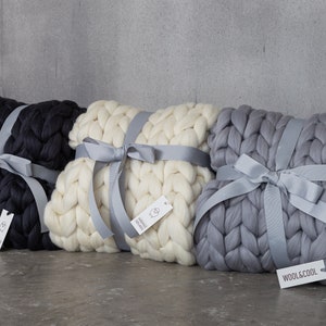 May include: Three chunky knit blankets in black, white, and gray are tied with gray satin ribbon. Each blanket has a small tag attached with the brand name "WOOL&COOL".