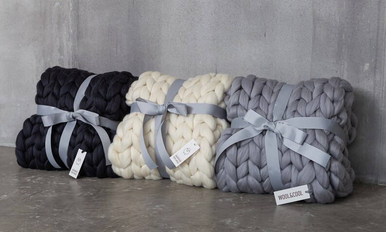May include: Three chunky knit blankets in black, white, and gray are tied with gray satin ribbon. Each blanket has a small tag attached with the brand name "WOOL&COOL".