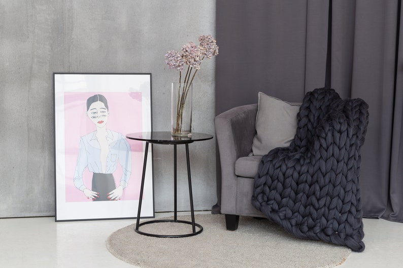 May include: A black side table with a round marble top sits in a living room with a gray armchair and a chunky knit throw blanket. A vase with dried flowers sits on the table.