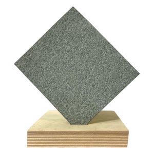 May include: A gray, textured, square-shaped stone sculpture is mounted on a layered wooden base. The stone is angled, creating a diamond shape. The wooden base has visible grain and a natural, light brown color.