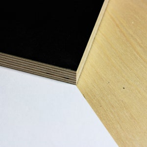 May include: Close-up of a black plywood sheet with visible layers, placed on top of a light brown plywood sheet.