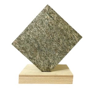 May include: A square, textured, gray-green stone is mounted on a rectangular, layered wooden base. The stone is angled, creating a dynamic visual. The wood base has visible grain and a light brown color. The background is white.