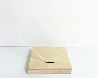 May include: A clear acrylic sheet standing upright on a wooden base. The base is made of multiple layers of plywood and has a small hole in the center.