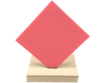 Könnte beinhalten: Ein leuchtend pinkfarbenes quadratisches Stück Acrylkunststoff auf einem Holzständer.