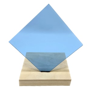 May include: A light blue square piece of acrylic glass is standing on a wooden base. The acrylic glass is translucent and has a slight blue tint.