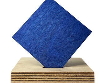 May include: A modern sculpture featuring a vibrant blue square set at an angle, mounted on a natural wood base. The blue square has visible wood grain, and the base is made of layered plywood. This abstract art piece is suitable for home decor.