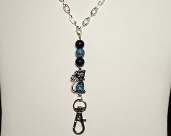 May include: A silver chain necklace with a black and blue cat charm and three black and blue beads. The necklace has a silver lobster clasp.