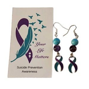 Pode incluir: Brincos de conscientização sobre a prevenção do suicídio em turquesa e roxo com um design de pena turquesa e ponto e vírgula em um cartão que diz "Your Life Matters" e "Suicide Prevention Awareness".