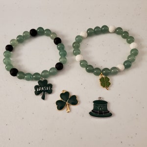Puede incluir: Dos pulseras de cuentas verdes con dijes. Una pulsera tiene cuentas negras y un dije de trébol con la palabra "IRISH" en él. La otra pulsera tiene cuentas blancas y un dije de trébol. Hay dos dijes adicionales: un trébol y un sombrero verde de duende.