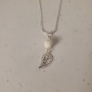 May include: A silver chain necklace with a white lava rock bead and a silver leaf pendant.