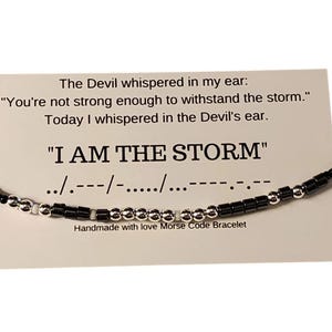 以下が含まれることがあります： 黒と銀のビーズブレスレット。メッセージは「The Devil whispered in my ear: "You're not strong enough to withstand the storm." Today I whispered in the Devil's ear. "I AM THE STORM"../.---/-...../...--- Handmade with love Morse Code Bracelet」です。