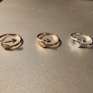 May include: Three adjustable arrow rings in gold, rose gold, and silver.
