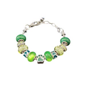 May include: A silver charm bracelet with green and yellow beads, including a paw print charm.