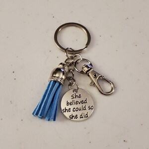 May include: A silver keyring with a blue tassel charm and a round silver charm with the text "She believed she could so she did".