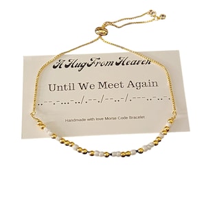 May include: Gold beaded bracelet with white beads and a sliding clasp. The bracelet has a card attached with the text "A Hug From Heaven" and "Until We Meet Again" in black text. The card also includes Morse code for the phrase "Until We Meet Again".