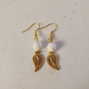 Könnte beinhalten: Ein Paar goldene Ohrringe mit weißen Lavasteinen und goldenen Blatt-Anhängern.