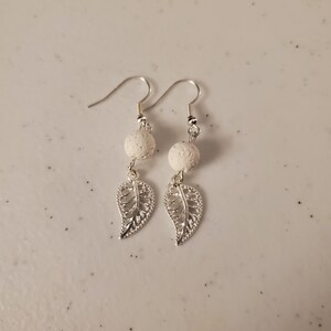 May include: A pair of silver earrings with white lava rock beads and delicate leaf charms.