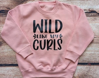 May include: A pink sweatshirt with the text "WILD LIKE MY CURLS" printed in black.