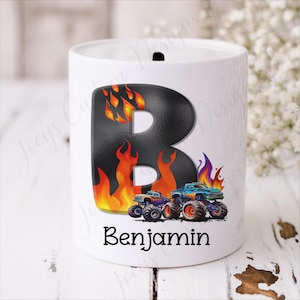 May include: White ceramic bank with a black letter "B" design, flames, and monster trucks. The name "Benjamin" is printed below the design. The bank has a slot on top for inserting coins.