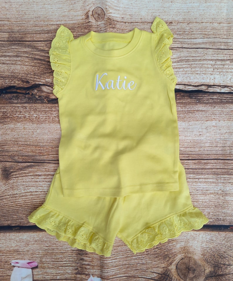 May include: Yellow sleeveless top and shorts set with white lace trim and the name "Katie" embroidered on the front of the top.