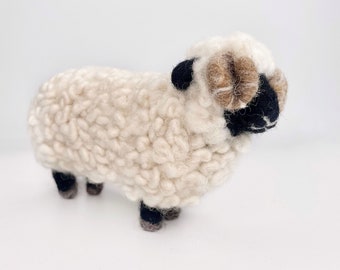 May include: A white wool sheep with brown horns and black eyes. The sheep is standing on a white surface.