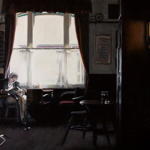 May include: A man sits in a chair by a window in a dimly lit pub, reading a book. The window is covered with white curtains and the room is decorated with dark wood and red curtains. There is a table with a glass of beer on it in the foreground.