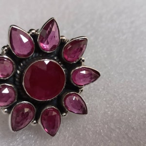 May include: A silver ring with a large, round, pink gemstone surrounded by eight smaller, teardrop-shaped pink gemstones.