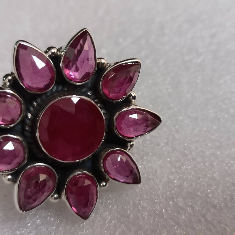 May include: A silver ring with a large, round, pink gemstone surrounded by eight smaller, teardrop-shaped pink gemstones.
