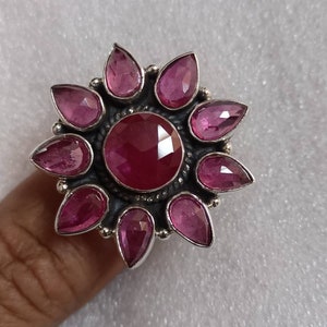 May include: A silver ring with a large pink gemstone surrounded by smaller pink gemstones in a flower shape.