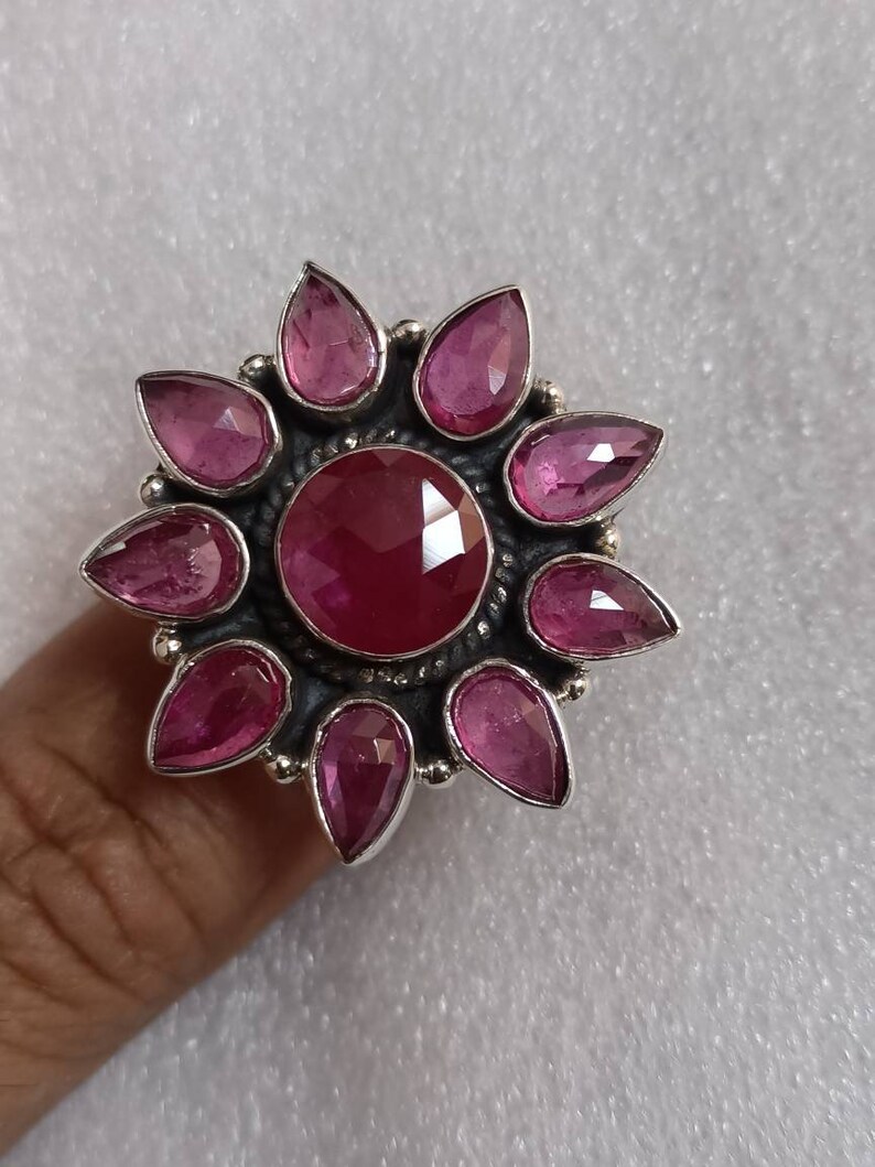 May include: A silver ring with a large pink gemstone surrounded by smaller pink gemstones in a flower shape.