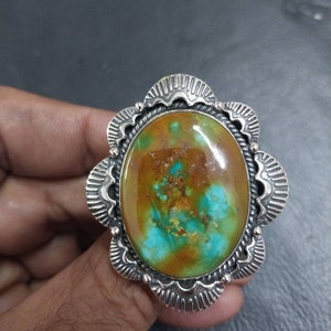 May include: A silver ring with a large oval turquoise stone set in a decorative silver bezel. The stone has a mix of green, blue, and brown colors.