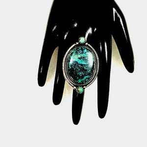 Może przedstawiać: Srebrny pierścionek z dużym owalnym turkusem i dwoma mniejszymi turkusami po bokach.