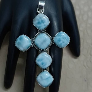 May include: A silver pendant in the shape of a cross with five blue and white gemstone accents.