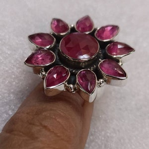 May include: A silver ring with a large pink gemstone surrounded by smaller pink gemstones. The ring is set in a flower design.